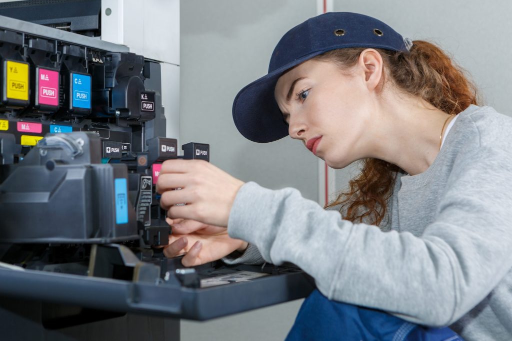 Technician installing or adjusting ink cartridges inside a large printer, focusing on the internal components.
