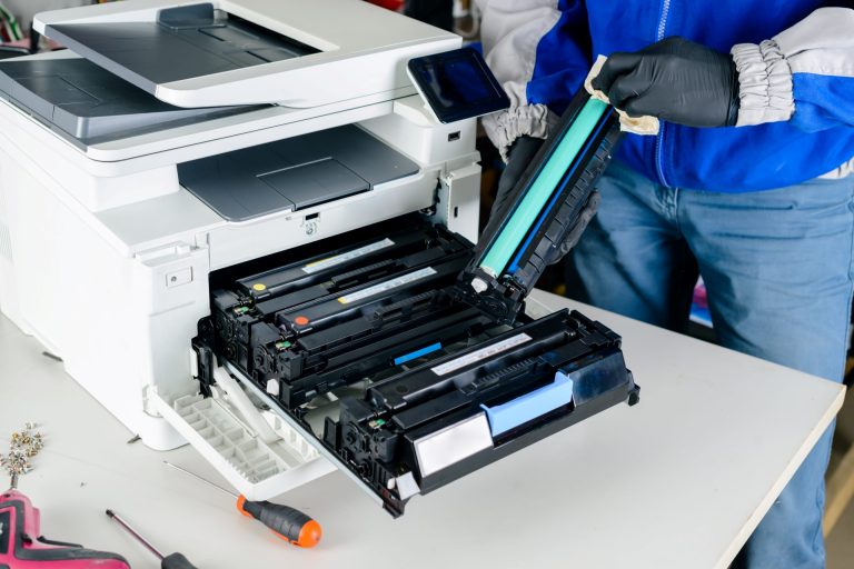Technician removing and cleaning a printer drum unit while replacing toner cartridges inside a multifunction printer.