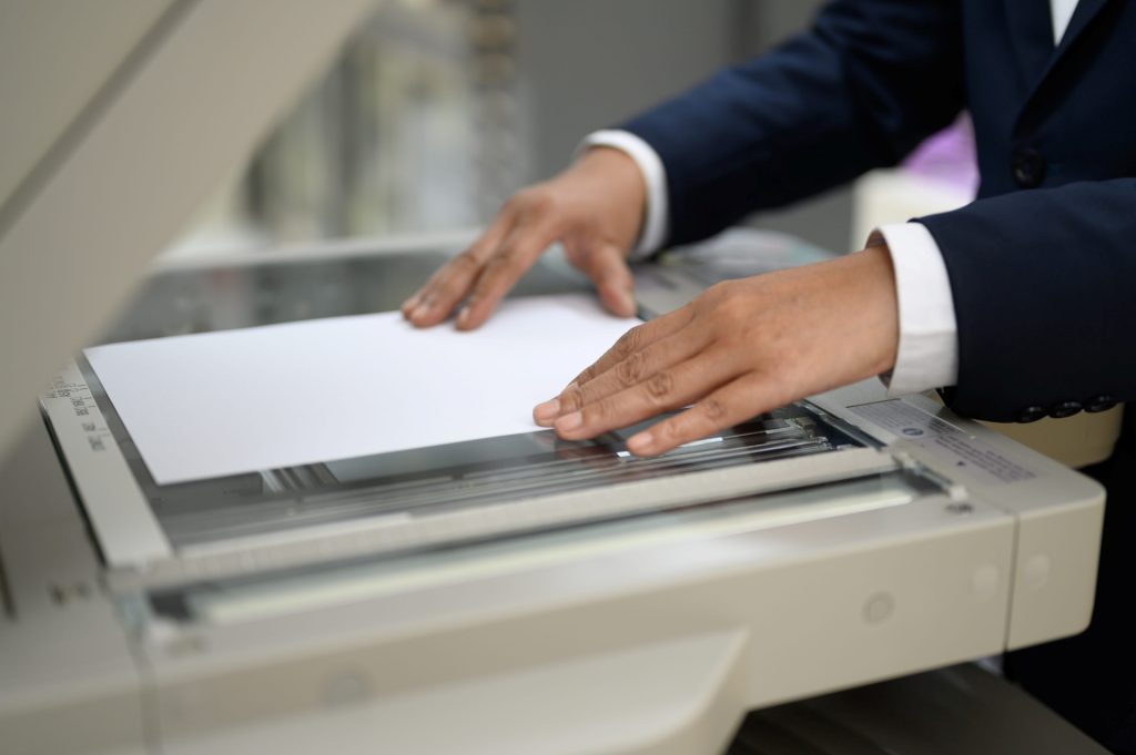 Person in a business suit placing a sheet of paper onto a photocopier or scanner, preparing to copy or scan a document.